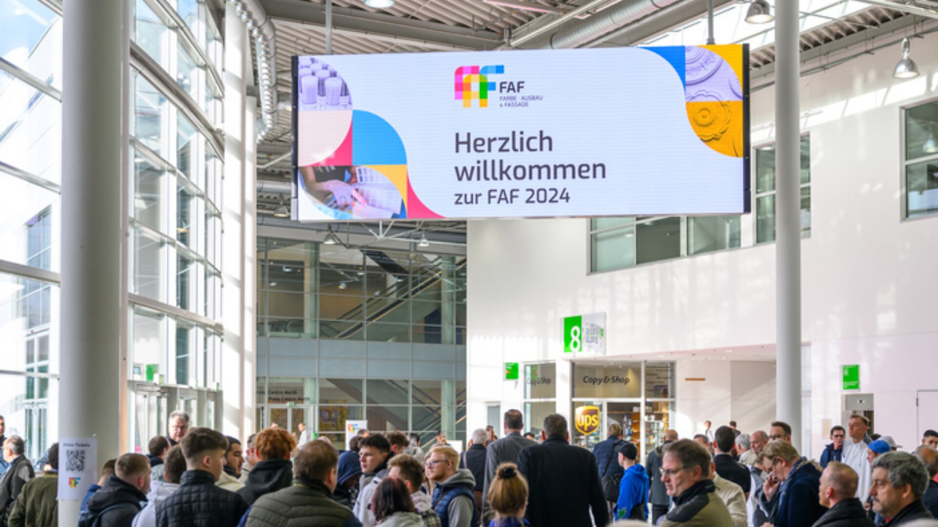 Eine Menschenmenge versammelt sich in einer hellen Kongresshalle unter einem großen Schild mit der Aufschrift Herzlich willkommen zur FAF 2024 am Eingang zu einer Veranstaltung.