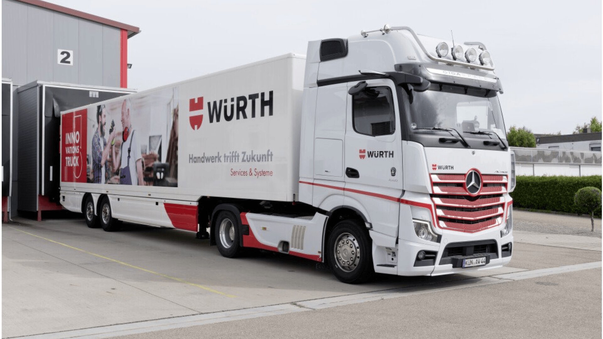 A large white Würth-branded Mercedes-Benz truck with red accents is parked at a loading dock. The truck features company logos and German text on the side, with a modern industrial building in the background.
