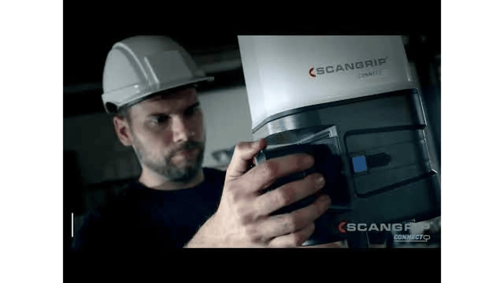 A man wearing a white safety helmet examines and adjusts a SCANGRIP CONNECT device, likely used for lighting or inspection in an industrial or work environment.