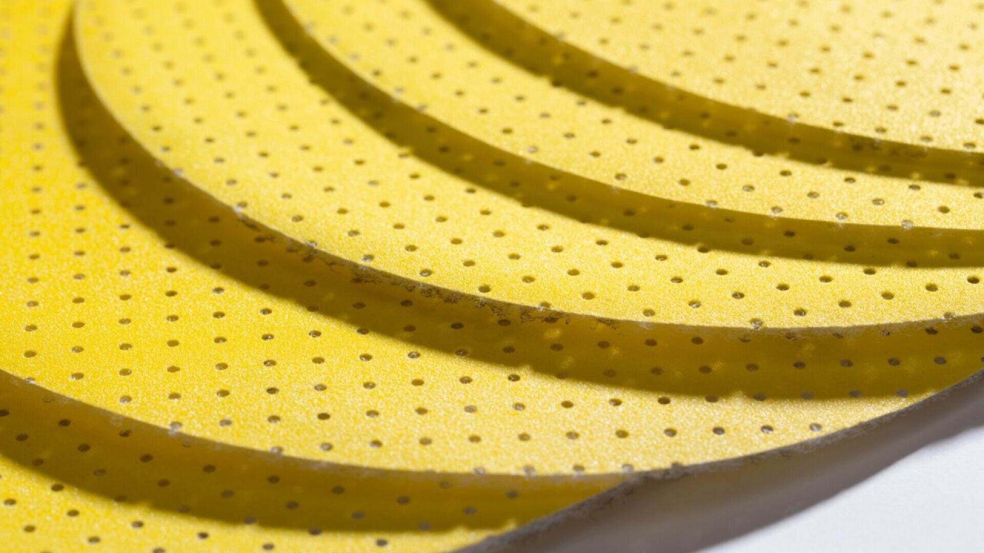 Close-up of several overlapping circular yellow sheets with small evenly spaced holes, arranged in a diagonal pattern. The surface appears textured and the lighting highlights the raised edges.