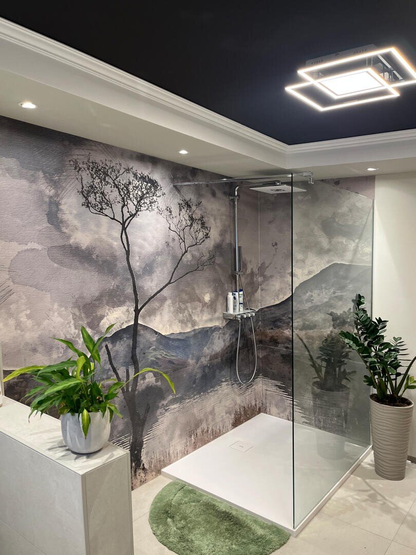 Modernes Badezimmer mit ebenerdiger Glasdusche und einem Wandbild mit einem Baum und einem Wolkenhimmel. Zwei grüne Topfpflanzen und ein runder grüner Teppich verleihen dem stilvollen, hellen Raum natürliche Akzente.
