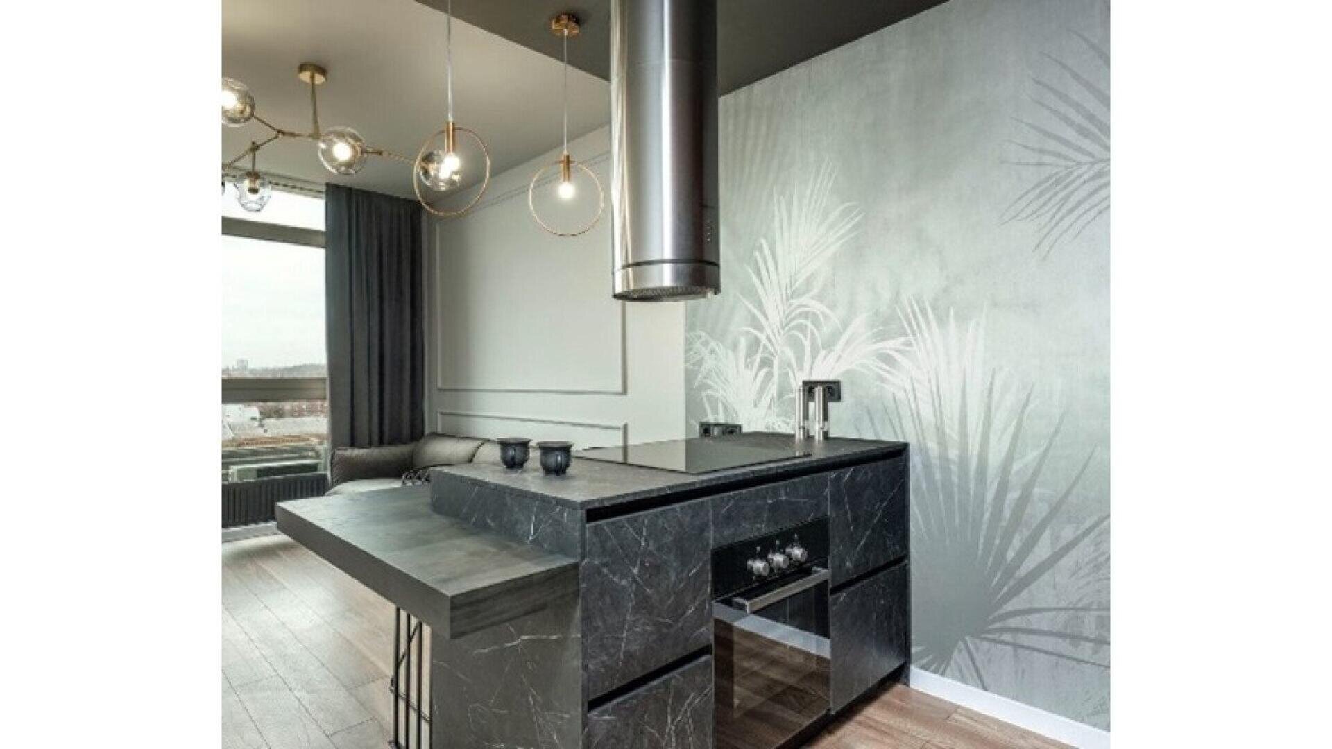 Modern kitchen with a black marble island, built-in oven, minimalist faucet, and pendant lighting. Light wood floors and a wall with subtle palm leaf patterns create a stylish, contemporary space.