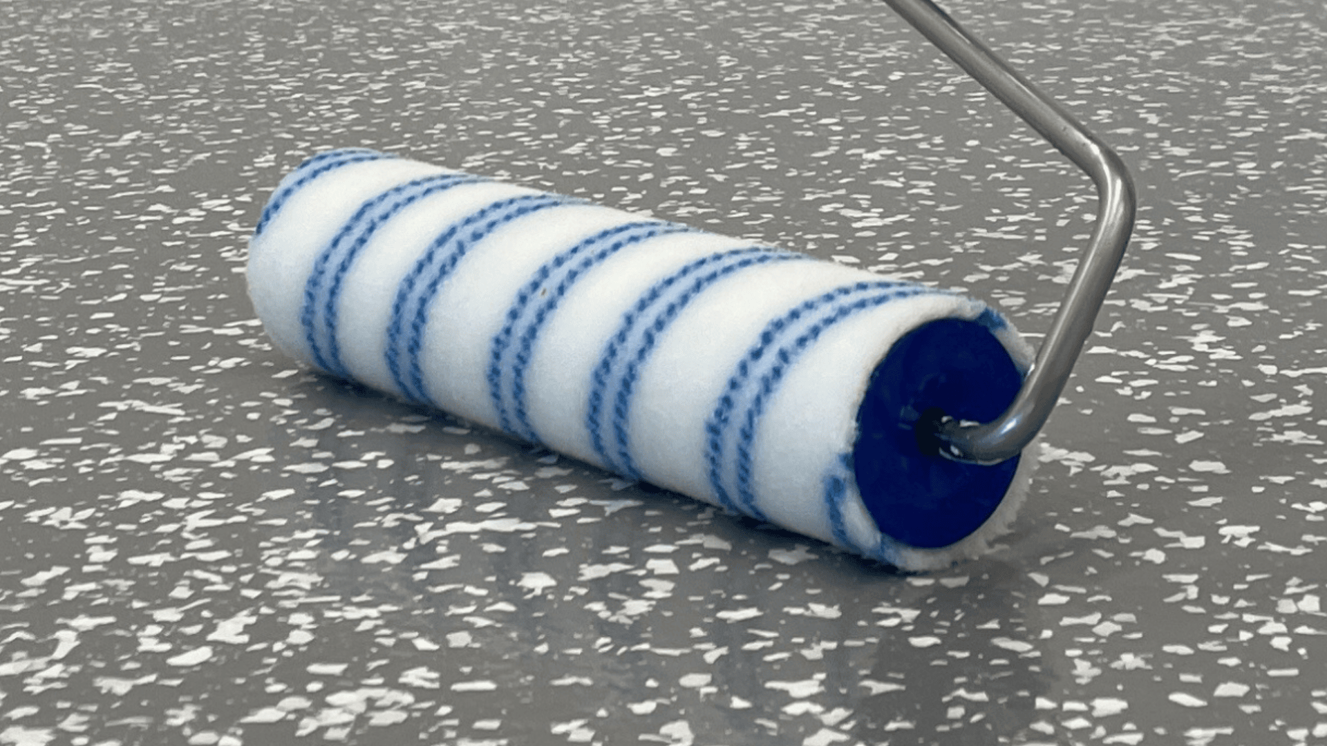 A close-up of a paint roller with white and blue stripes resting on a gray, speckled surface.