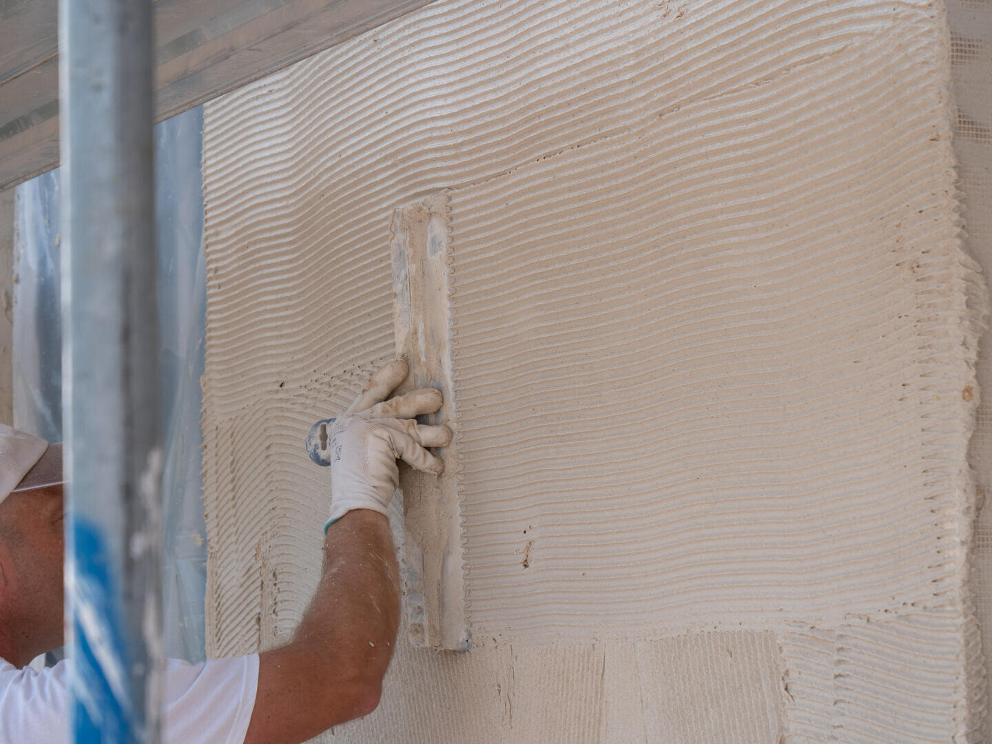A person wearing a white glove smooths plaster on a wall with a trowel, creating an even textured surface during construction or renovation work.