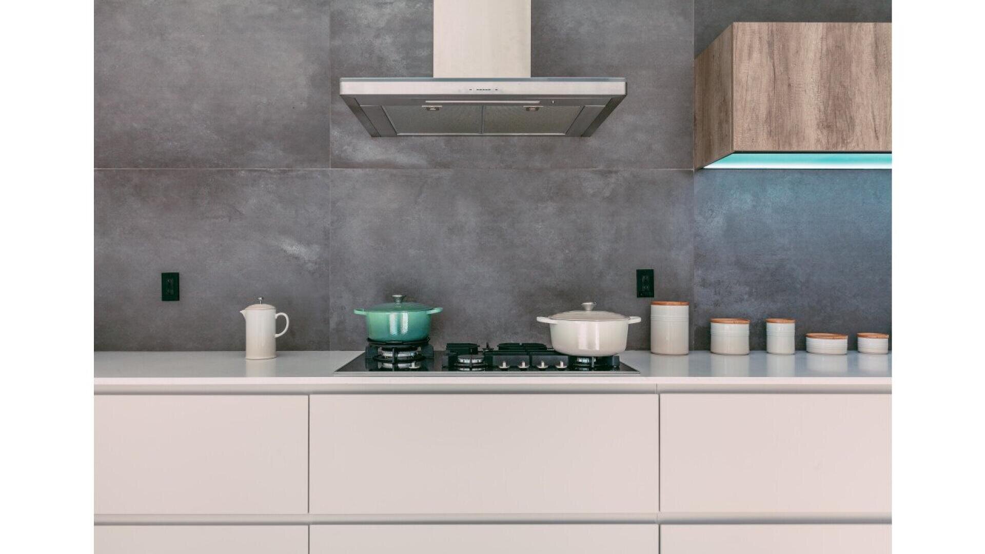 Modern kitchen with gray walls, white cabinets, a stove with a green and a white pot, a white teapot, and six ceramic containers on the countertop beneath a stainless steel range hood.