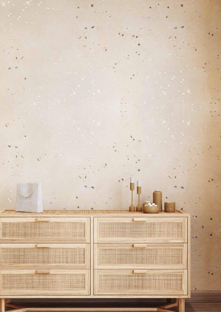 A light wood dresser with six drawers stands against a speckled beige wall. On top, there are candles, a small dish, and a light-colored bag. The style is minimalist and natural.