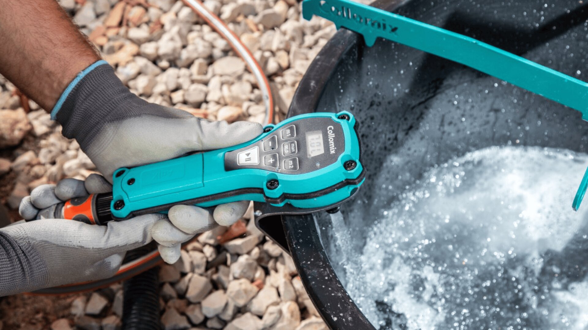 A gloved hand holds a blue digital water meter with a display, measuring water quality in a black container filled with swirling water and bubbles. Gravel is visible in the background.