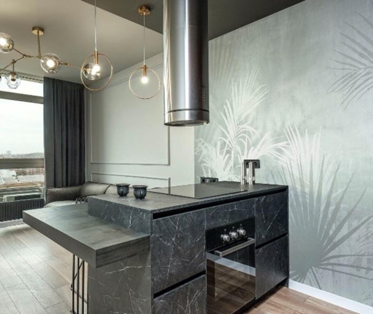 Moderne Küche mit schwarzen Marmoroberflächen, eingebautem Backofen, hängender Dunstabzugshaube und Frühstücksbar. Der Raum verfügt über Holzboden, ein großes Fenster, ein graues Sofa und eine Wand mit Blattmuster.